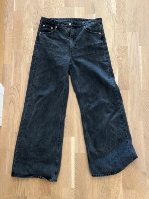 Svarta wide leg jeans weekday ace - Säljer ett par svarta jeans med breda ben och hög midja. Klassisk femficksmodell med raka sömmar och knappgylf. Jeansen har en avslappnad passform och är tillverkade i kraftigt denimtyg. Perfekta för en trendig och bekväm stil.