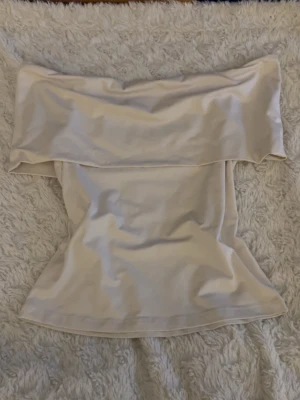 Beige axelbandslös topp från H&M - Säljer en beige axelbandslös topp från H&M. Toppen har en bred volang upptill som ger en snygg offshoulder-look och är figurnära i modellen. Perfekt att styla med jeans eller kjol för en trendig outfit.