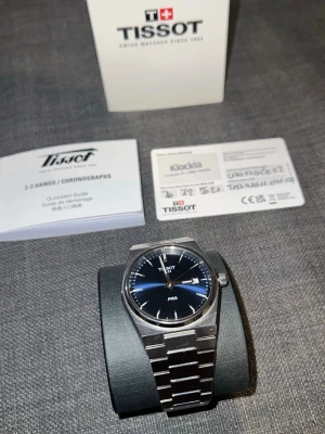 Tissot PRX - Fullset herrklocka i rostfritt stål - Nästa ny skick! Snygg Tissot herrklocka med länkarmband i rostfritt stål. Klockan har en klassisk, stilren design med silverfärgad finish och robust metallarmband. Perfekt accessoar för dig som gillar tidlös och elegant stil. Extra länkar ingår. Låda, bok och garanti kort också! 