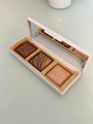 Trio Contour / Bronzer / highlighter Palette  - En smidig ansiktspalett i nyansen Deep. Paletten innehåller tre bakade produkter: en matt bronzer (Matt Golden Deep), en skimrande bronzer (Bronze Glow) och en highlighter (Rose Gold). Innehåller en inbyggd spegel och passar perfekt för att skulptera ansiktet och ge en solkysst lyster.