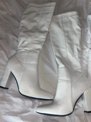 Vita höga stövlar med blockklack - Snygga vita stövlar med högt skaft och bred blockklack. Tillverkade i ett material med diskret rutmönster som ger en cool textur. Perfekta för att lyfta vilken outfit som helst med sin trendiga look och stilrena design. Använda 2 gånger, så små slitna på vissa ställen, men fortfarande i fint skick🤗🥰