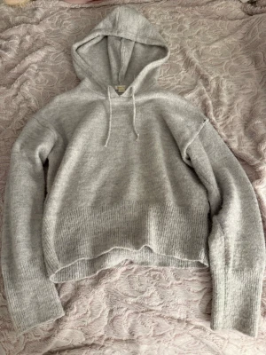 Ljusgrå hoodie från Gina Tricot - Mysig ljusgrå hoodie från Gina Tricot med huva och dragsko. Tröjan är stickad i ett mjukt material och har ribbade muddar vid ärmslut och nederkant. Perfekt för en avslappnad och chill stil.