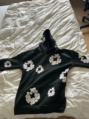 Svart denim tear set - Mysigt loungewear set i svart med stora vita blommönster. Setet består av en hoodie med magficka och matchande byxor med resår i midjan. Perfekt för chill dagar hemma. Materialet ser ut att vara mjukt och skönt, troligen bomull eller bomullsblandning.