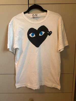  Comme des Garçons Play t-shirt - Köpt på farfetch runt 2 år sen för 1200kr.    Säljer en vit t-shirt från Comme des Garçons Play med det ikoniska svarta hjärtat med ögon tryckt på bröstet. T-shirten har rund hals och korta ärmar. Tillverkad i mjuk bomull som känns skön mot huden. Perfekt för dig som gillar streetwear och stilrena prints.