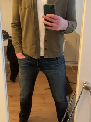 Olivgrön overshirt från Morris - Säljer en stilren olivgrön overshirt från Morris. Skjortan har lång ärm, klassisk krage, bröstficka och knappar framtill. Tillverkad i mjuk bomull som ger en avslappnad men snygg look. Perfekt att bära öppen över en t-shirt. Säljer den eftersom jag har vuxit ur den.