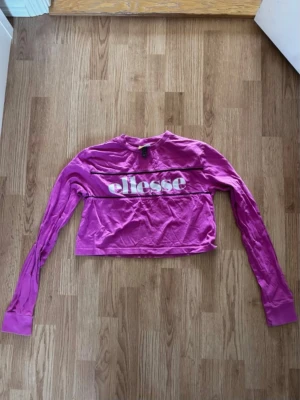 Rosa croppad långärmad topp Ellesse - Säljer en rosa croppad långärmad topp från Ellesse med vit logga framtill. Toppen har rund halsringning och är gjord i mjuk bomull. Perfekt för dig som gillar sportig och trendig stil.