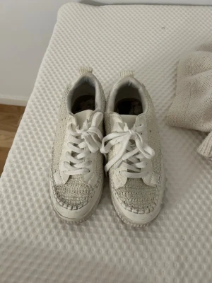 Vita flätade sneakers med platåsula - Säljer ett par vita sneakers med snygg flätad textil på sidorna och tåpartiet. Skorna har vita snören, platåsula och detaljer i vitt konstläder. Perfekta för dig som gillar en unik och trendig stil.