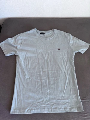 Vit t-shirt från Tommy Hilfiger - Klassisk vit t-shirt från Tommy Hilfiger med rund halsringning och liten broderad logga på bröstet. T-shirten har korta ärmar och är tillverkad i mjuk bomull, perfekt för en clean och stilren look.