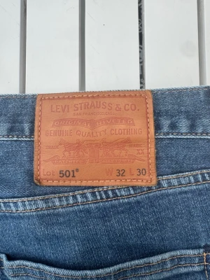 Levi's 501 blå raka jeans - Klassiska blå Levi's 501 jeans med rak passform och fem fickor. Jeansen har den ikoniska läderlappen bak i midjan och är tillverkade i slitstark denim. Perfekta för en avslappnad och tidlös stil.