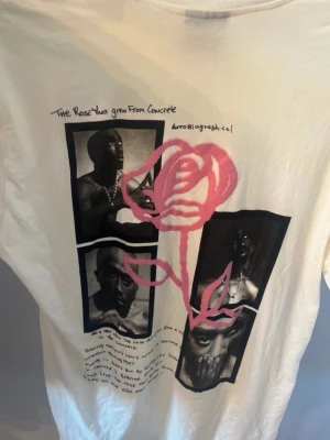 Tupac t-shirt - Vit creme Tupac 2pac t-shirt med svartvitt fototryck och en stor rosa ros på framsidan. Trycket innehåller tre porträttbilder och texten 'The Rose that grew from Concrete'. T-shirten har rund hals och korta ärmar, perfekt för en avslappnad stil. Storlek XS men väldigt stor så snarare L. Köpt för kanske 8€ i Spanien. 
