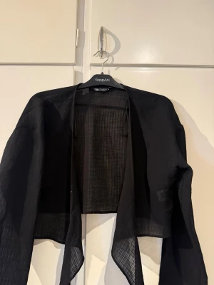 Svart transparent cardigan från Zara - Snygg svart cardigan från Zara i transparent, lätt material. Öppen framtill med avslappnad passform och långa ärmar. Perfekt att slänga över en topp för en cool layering-effekt.