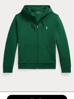Grön hoodie från Polo Ralph Lauren - Snygg grön hoodie från Polo Ralph Lauren med dragkedja, huva med dragsko och klassisk vit logga på bröstet. Tillverkad i mjukt material och har två fickor framtill. Perfekt för en chill och stilren look.