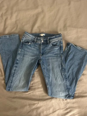 Ljusblå bootcut jeans med broderi - Säljer ett par ljusblå bootcut jeans med snygga broderade detaljer på bakfickorna. Klassisk femficksmodell och normal passform. Perfekta till sneakers eller boots för en avslappnad look.