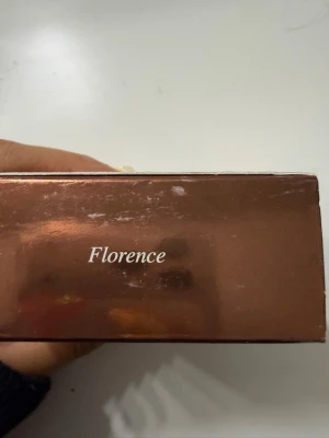 CAIA Loose Glow Bronzer Florence - Säljer en CAIA Loose Glow Bronzer i nyansen Florence. Förpackningen är fyrkantig och har en glansig, kopparfärgad finish. Produkten är ett löspuder som ger glow och värme till ansiktet. Perfekt för att skapa en solkysst look.