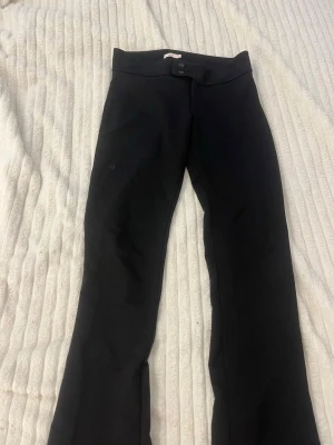 Svarta bootcut-byxor från Nelly - Säljer ett par svarta kostym bootcut-byxor från Nell med två knappar framtill. Byxorna har en smal passform upptill och utsvängda ben. Perfekta för en trendig och stilren look. 