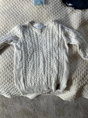 Vit kabelstickad tröja - Kabelstickad tröja i mjuk vit bomull med klassiskt flätmönster både fram och bak. Rund halsringning och ribbade muddar vid ärmslut och nederkant. Perfekt för lager på lager och en stilren look.