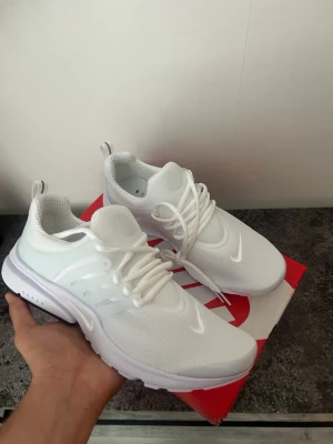 Nike vita mesh sneakers - Fräscha vita sneakers från Nike med mesh-ovandel och plastdetaljer på sidorna. Skorna har en låg silhuett, vita snören och diskreta swoosh-loggor på tå och sida. Perfekta för en clean och sportig look.