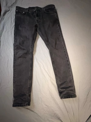 Svarta jeans från Nudie Jeans - Säljer ett par svarta lean Dean jeans från Nudie Jeans med klassisk femficksmodell och dragkedjegylf. Jeansen har en tvättad look och är tillverkade i mjuk bomullsdenim. Perfekta för dig som gillar en smalare passform och stilren design. Storleken är 30w/30L