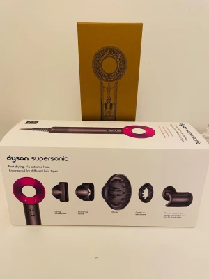 Dyson Supersonic hårfön - Nypris 6000kr.                                                      Säljer en Dyson Supersonic hårfön i snygg grå och rosa design. Kommer med flera olika munstycken för styling, diffuser och koncentrator. Hårfönen är tillverkad i plast och metall och har en modern, rund form. Perfekt för snabb och skonsam hårtorkning.