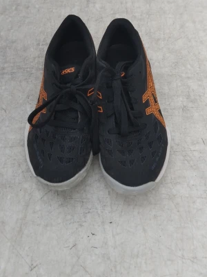 Svarta Asics inomhusskor med orange detaljer - Säljer ett par svarta inomhusskor från Asics med orange logga och detaljer. Skorna har ventilerande meshmaterial upptill och slitstarka, mönstrade sulor i vitt och grått för bra grepp på inomhusgolv. Perfekta för sporter som innebandy eller handboll. Pris kan diskuteras