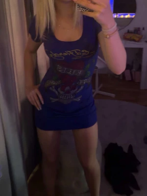 Blå ed Hardy klänning - Snygg blå kortklänning med coolt tryck framtill och snörning i ryggen. Klänningen har korta ärmar och en tight passform som framhäver figuren. Perfekt för dig som vill sticka ut med en unik detalj på ryggen. 