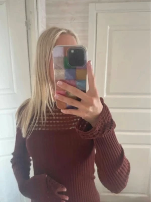 Vinröd ribbstickad tröja från ASOS - Säljer en brun ribbstickad tröja från ASOS DESIGN med lång ärm och dekorativa detaljer vid ärmslut och hals. Tröjan har ett diskret mönster upptill och är figurnära i modellen. Perfekt för dig som gillar en stilren och mysig look.