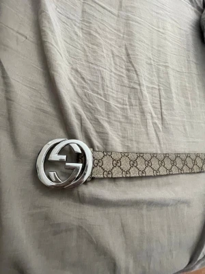 Beige bälte - Snyggt beige bälte med klassiskt mönster och stor rund silverspänne. Perfekt accessoar för att lyfta din outfit med en lyxig touch. Bältet har en stilren design och passar till många olika looks.lite använd 