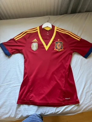 Spaniens landslagströja Adidas röd - Säljer en röd fotbollströja från år 2010 Spanien inget namn på ryggen tyvärr. Köpt på unisport för cirka 2 år sedan ny pris idag  1199 men köpte då för 899. Säljer den för 350 kr aldrig använd. Storlek s men funkar på xs också 