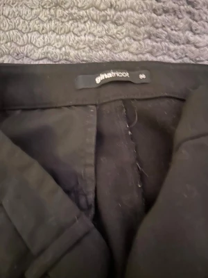 Svarta kostymbyxor Gina Tricot - Stilrena svarta kostymbyxor från Gina Tricot i rak modell med hög midja och hällor för skärp. Perfekta för en clean och snygg look. Materialet känns mjukt och följsamt, vilket gör dem bekväma att bära hela dagen.