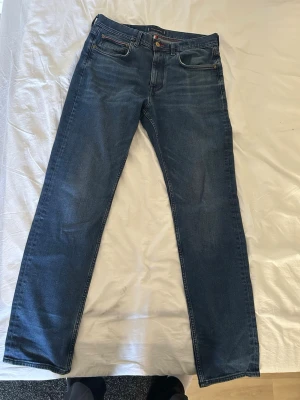 Mörkblå raka jeans - Säljer ett par mörkblå jeans med rak passform och klassisk femficksdesign. Jeansen har subtila slitningar och kontrastsömmar. Perfekta till en avslappnad stil och passar till det mesta i garderoben.