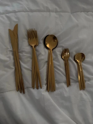  bestickset  - Säljer ett stilrent bestickset i guldigt metall med knivar, gafflar, matskedar, dessertgafflar och teskedar. Modern design med slimmad form som ger en lyxig känsla till dukningen. Perfekt för dig som vill ha något extra till matbordet. 6 st av varje så totalt 30 st bestick 