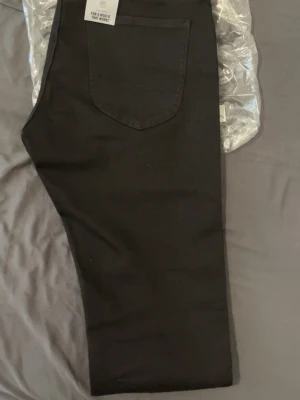 slim tapered jeans från Lee - Snygga svarta jeans från Lee med klassisk femficksmodell och raka ben. Jeansen har silverfärgade nitar och knapp, samt Lee-logga på linningen. Tillverkade i ett mjukt och slitstarkt denimtyg som passar perfekt till alla tillfällen.