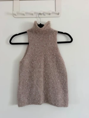 Beige stickad ärmlös halter topp - Säljer en beige stickad ärmlös polotröja med diskreta prickar i materialet. Tröjan har hög krage och är gjord i ett mjukt, fluffigt material som ger en mysig känsla. Perfekt att styla över en skjorta eller t-shirt för en trendig lager-på-lager-look. Sparsamt använd. Storlek S men passar även xs (jag själv har xs och den passar mig perfekt)
