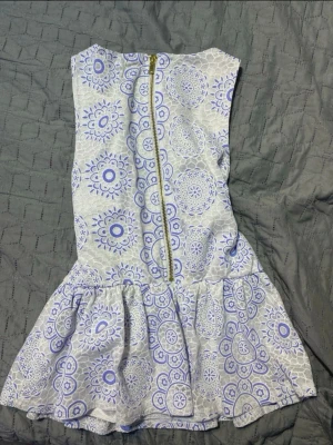 Vit blommig blus med volang - Säljer en vit blus med blått blommigt mönster och volang nedtill. Blusen är ärmlös och har en synlig dragkedja bak. Materialet känns som bomull med spetsdetaljer och den har en normal passform. Perfekt för dig som gillar unika detaljer och somriga vibes.