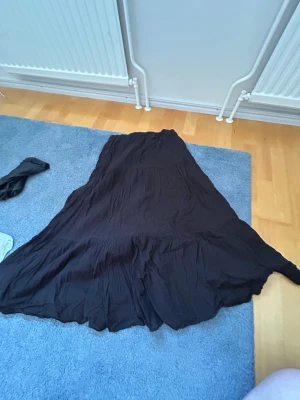 Svart långkjol med resårmidja - Säljer en svart långkjol med skön resår i midjan. Kjolen har en luftig och flowy passform med lätt skrynklat tyg som ger en avslappnad vibe. Perfekt att styla med en crop top eller stickad tröja för en chill look.