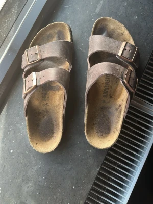 Bruna Birkenstock sandaler i mocka - Säljer ett par klassiska Birkenstock sandaler i mörkbrun färg, De är i bra skick och säljes pgr av att jag växt ur dom. 