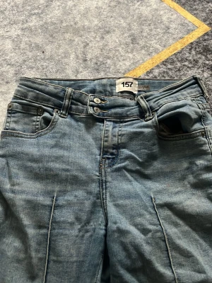 Ljusblå raka jeans med dubbla knappar - Säljer ett par ljusblå jeans med raka ben och dubbla knappar i midjan. Jeansen har klassiska fem fickor och markerade sömmar framtill. Materialet är denim i bomull och passformen är avslappnad och trendig.
