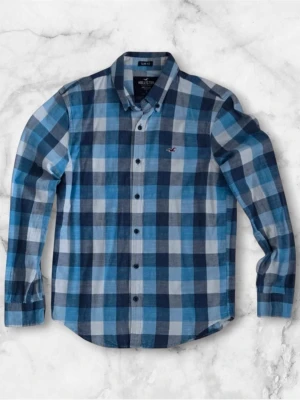 Blå rutig skjorta från Hollister - Snygg blå och vit rutig skjorta från Hollister med klassisk krage och knäppning framtill. Skjortan har lång ärm och en liten logga broderad på bröstet. Perfekt för dig som gillar en avslappnad men ändå stilren look.
