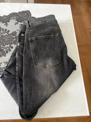 Grå tvättade raka jeans - Säljer ett par grå tvättade jeans med rak passform och klassisk femficksdesign. Jeansen har en snygg sliten look med ljusare partier på låren och bakfickan. Perfekta för en avslappnad och trendig stil. Materialet är denim i bomull.