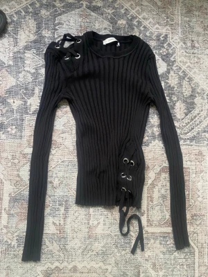 Zara topp - Trendig svart ribbstickad tröja från Zara med långa ärmar och coola snörningsdetaljer vid axeln och midjan. Tight passform, storlek S men även xs