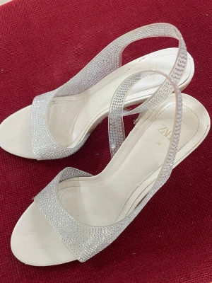 Glittriga klackar  med öppen tå från ZARA - Säljer ett par eleganta klackar från ZARA i storlek 36. Skorna är glittriga på remmarna och har öppen tå samt smal klack. Har används någon enstaka gång men finns viss slitage på dem. De är i storlek 36 men funkar även för mig som har storlek 38 men en aning små då