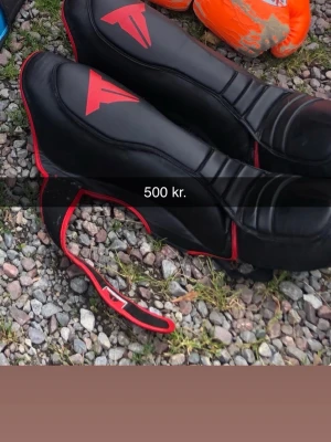 Svarta och röda sparksskydd - Säljer ett par svarta sparksskydd med röda detaljer och logga. De har en sportig design med kardborreband för enkel justering och sitter stabilt på foten. Perfekta för kampsport eller träning där extra skydd behövs.