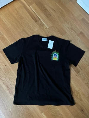 Casablanca T-shirt  - Säljer en svart t-shirt från Casablanca med färgglad tryckt grafik och texten 'Avenida Casablanca' på bröstet. Klassisk passform med rund hals och korta ärmar. Perfekt för dig som vill ha en stilren men ändå unik look.