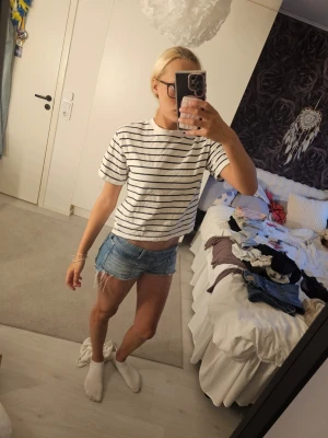 Vit randig croppad t-shirt - Säljer en vit croppad t-shirt med svarta horisontella ränder. T-shirten har korta ärmar och en avslappnad passform. Perfekt till jeansshorts eller kjol för en enkel och stilren look. Från gina tricot!