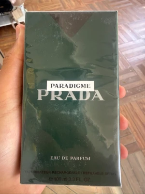 Prada Paradigme Eau de Parfum 100ml - Prada Paradigme Eau de Parfum i en elegant mörkgrön rektangulär förpackning. Flaskan rymmer 100 ml och är en påfyllningsbar spray. Lyxig doft från Prada, perfekt för dig som vill ha något exklusivt i parfymhyllan.
