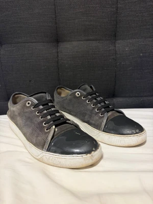 Lanvins, uk 8/42/43 - Snygga sneakers i grått tyg med svarta skosnören och en glansig svart tådel i läderlook. Skorna har vita sulor och metallfärgade öljetter. Perfekta för en avslappnad streetstyle.