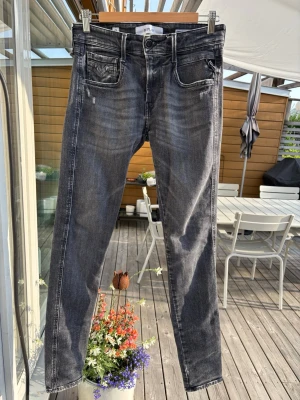 Replay Anbass Jeans Grå - Snygga gråa Replay Anbass slim fit jeans med lätt slitna detaljer och tvättad look. Jeansen har klassiska fem fickor och raka ben. Perfekta för en avslappnad och trendig stil. Storlek W28/L32. Hör av dig vid frågor!