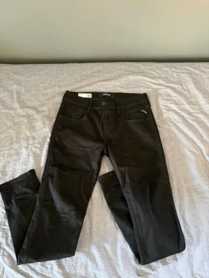 Replay Anbass - Säljer ett par svarta slim fit jeans från Replay med klassisk femficksmodell och dragkedjedetalj vid fickan. Jeansen har raka ben och bälteshällor. Materialet är stretchigt för extra komfort och passform.