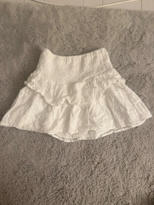 Vit volangkjol från gina  - Söt vit kortkjol med smock i midjan och dubbla volanger. Kjolen har diskret prickigt mönster och är gjord i ett lätt bomullstyg som passar perfekt till sommaren. Jättefin med t.ex. en beige stickad tröja. Den är storlek 152 men jag är 164 och sen passar Perfekt 