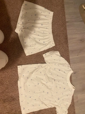 Vit pyjamas med blått blommönster - En söt matchad pyjamas med shorts och en T-shirt till. I färgen vit med blåa blommor som detalj, helt ny aldrig använt.💕